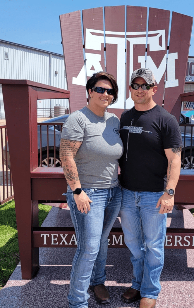 Two individuals posing in front of a texas a&m university sign.