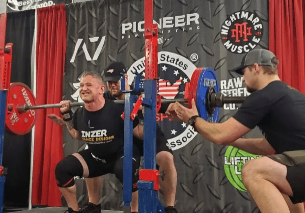 A powerlifter performing a squat at a competition with spotters ready to assist.