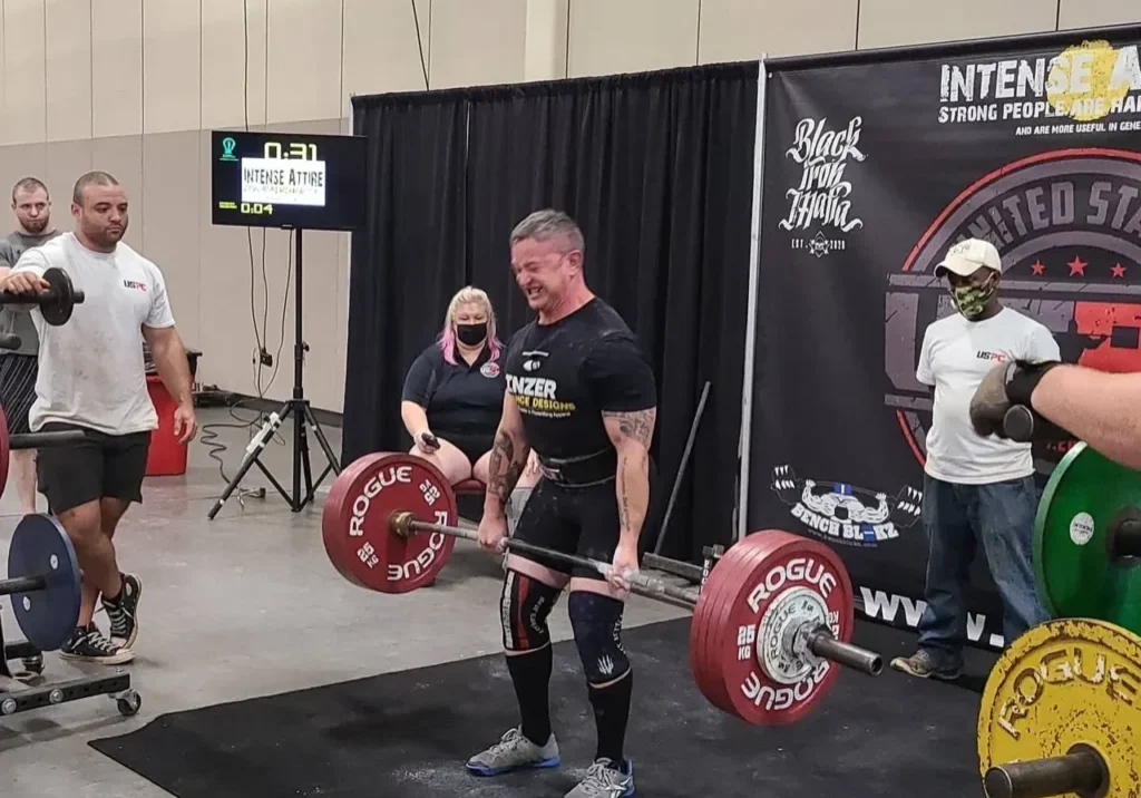 A man lifting some heavy barbells in front of other people.